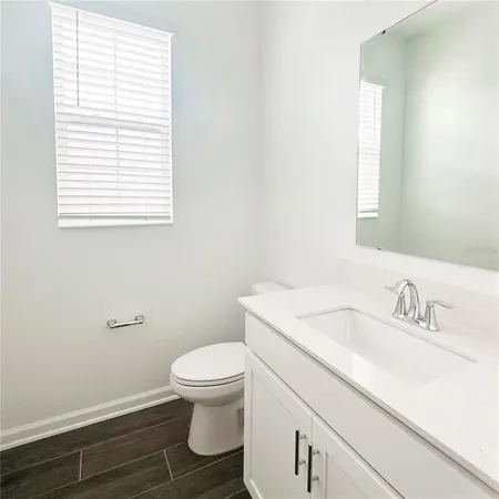 a bathroom with a granite countertop toilet a sink a mirror and a window