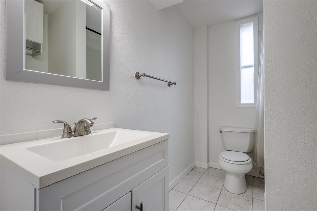 2309 Wesley Street, Unit B Greenville, TX 75401 - Photo 15 of 27 a bathroom with a toilet a sink a mirror and a window