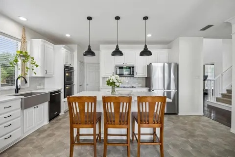 a kitchen with stainless steel appliances kitchen island granite countertop a dining table chairs and white cabinets