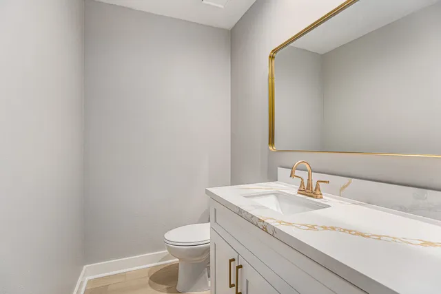 a bathroom with a granite countertop sink vanity mirror and toilet