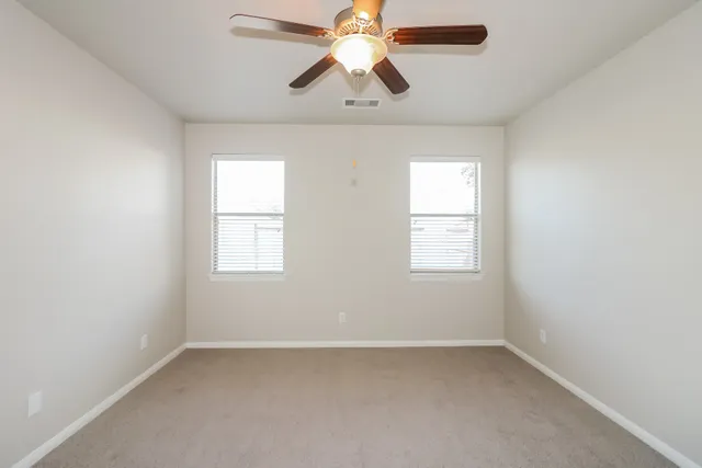 an empty room with chandelier fan and windows
