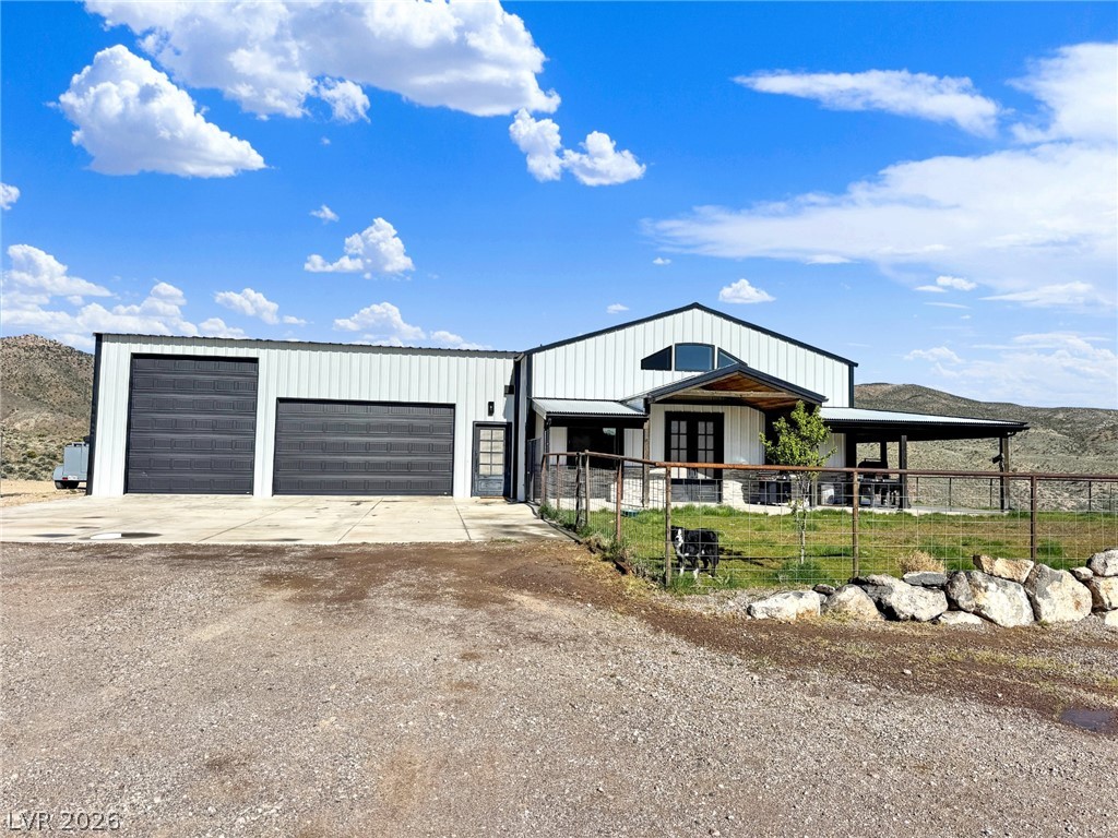 9393 North 93rd Highway Caliente, NV 89008 - Photo 7 of 41 A modern rural retreat boasts expansive garage space and a welcoming covered entry, nestled against a scenic mountain backdrop.
