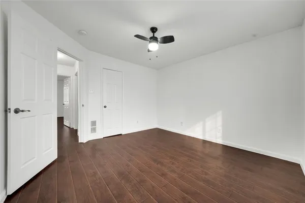 an empty room with wooden floor ceiling fan and windows