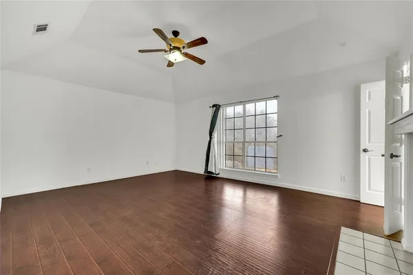 an empty room with wooden floor fan and windows