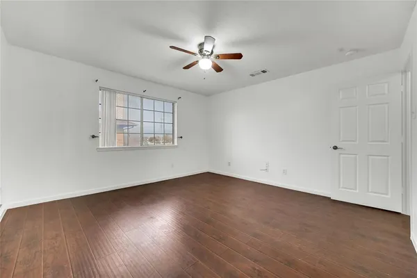 an empty room with wooden floor fan and windows