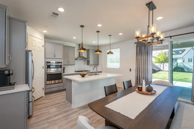 a large kitchen with granite countertop a stove a sink a refrigerator a microwave a dining table and chairs with wooden floor