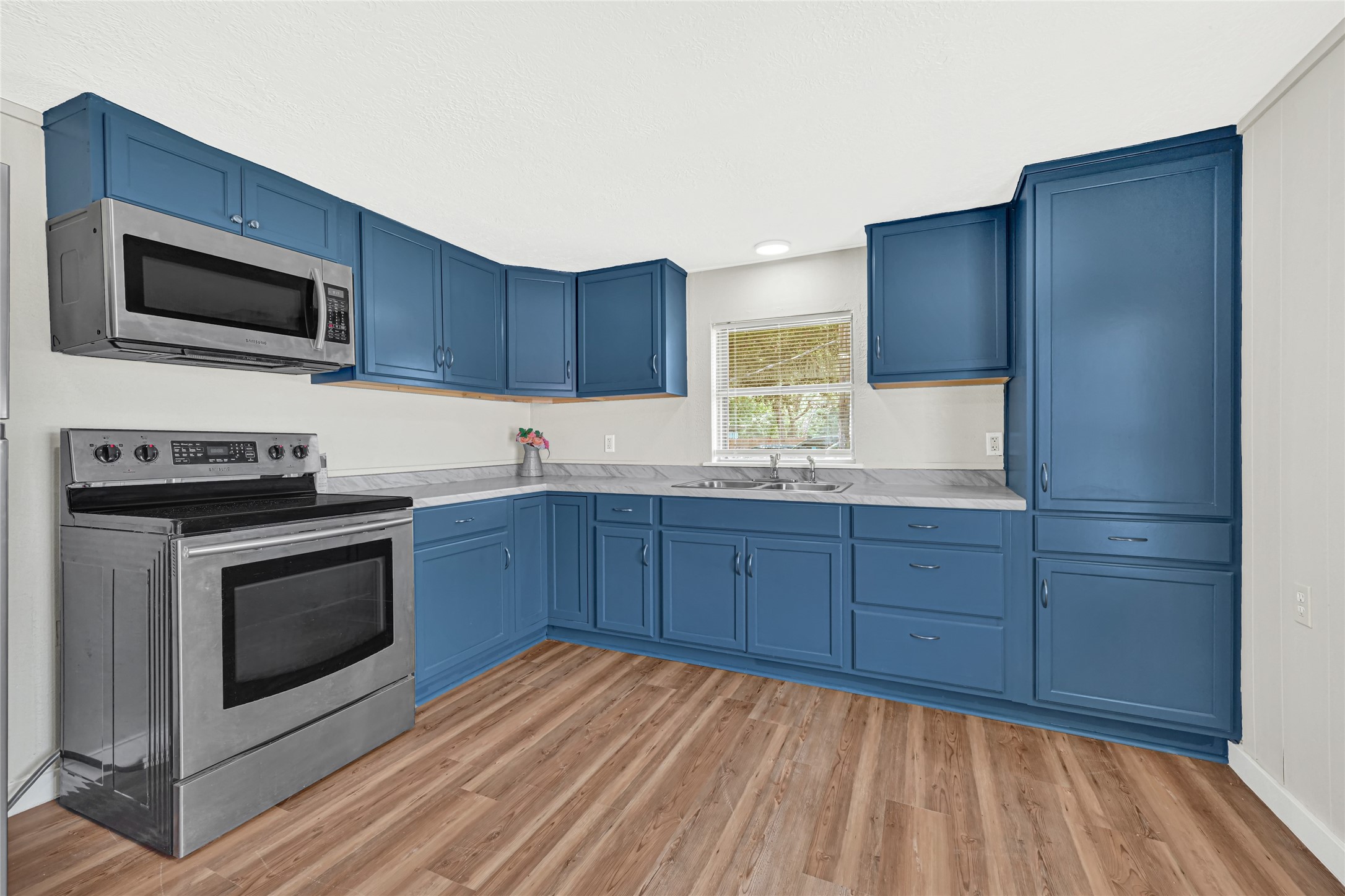 4568 Dunnam Road, Unit B Houston, TX 77345 - Photo 5 of 15 Bright kitchen with striking blue cabinetry, modern stainless-steel appliances, and laminate wood flooring.