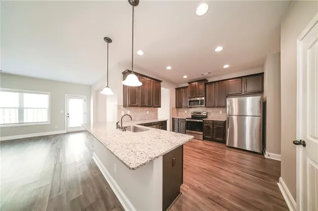 a kitchen with stainless steel appliances granite countertop a refrigerator a sink dishwasher a stove and white countertops with wooden floor