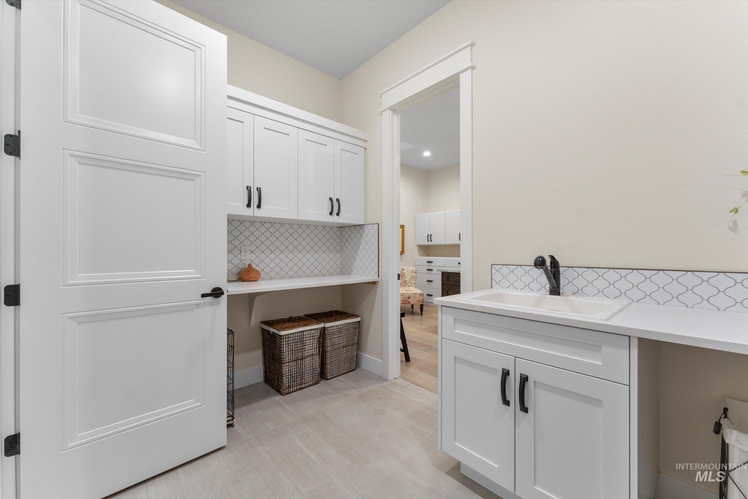 6585 South Pemberley Way Meridian, ID 83642 - Photo 37 of 43 Laundry room with white shaker cabinetry, patterned tile backsplash, light-toned flooring, and a utility sink with a matte black faucet