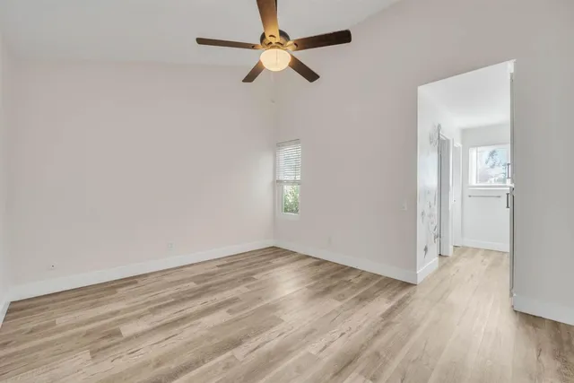 an empty room with wooden floor ceiling fan and windows