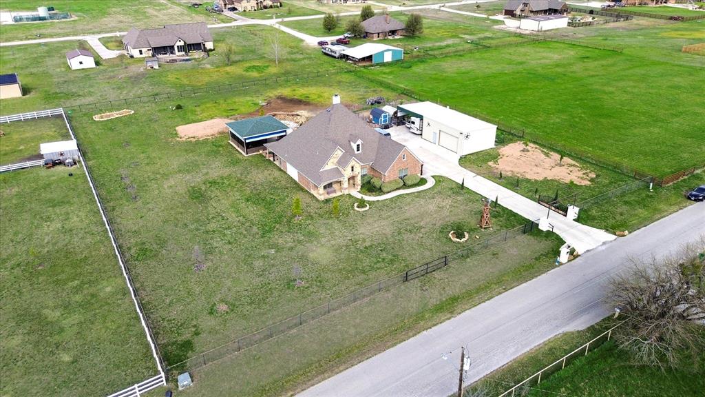 119 George Owens Road Ponder, TX 76259 - Photo 25 of 26 Spacious property featuring a brick-clad residence with a multi-gabled roofline, an expansive green lawn, an attached covered patio, a detached garage structure, and a concrete driveway