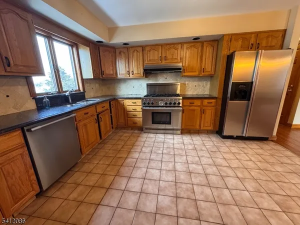 a kitchen with stainless steel appliances a sink a stove a refrigerator cabinets and a window