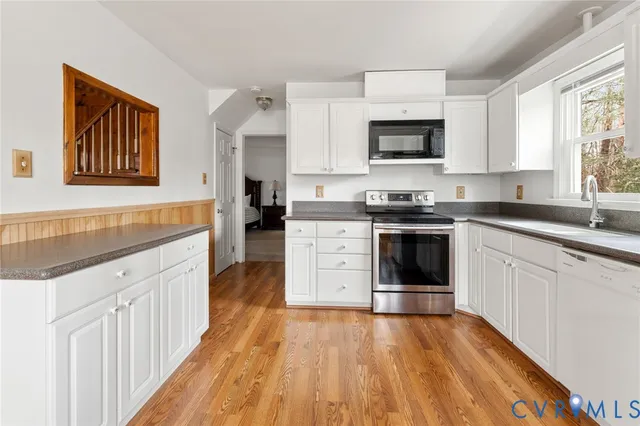 a kitchen with stainless steel appliances granite countertop a stove top oven a sink dishwasher and white cabinets with wooden floor