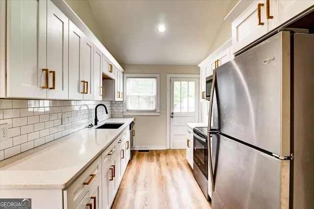a kitchen with granite countertop a refrigerator a sink a stove and white cabinets with wooden floor