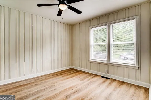 an empty room with wooden floor fan and windows