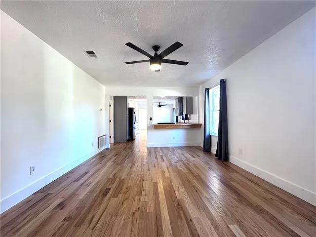 a view of a big room with wooden floor a ceiling fan and windows