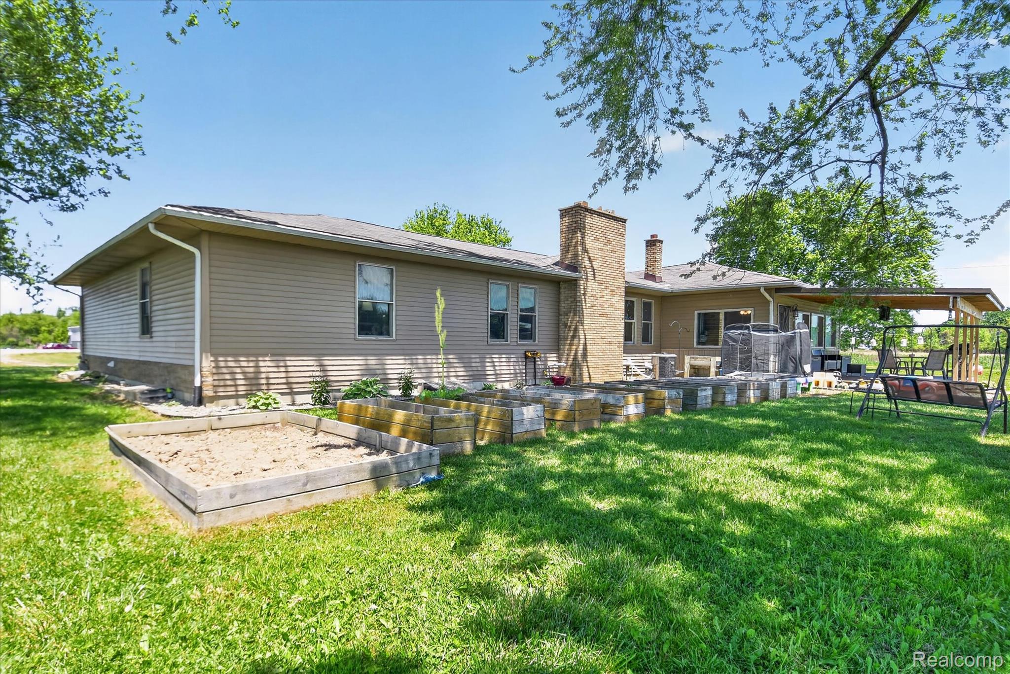 3949 West Burns Line Road Brown City, MI 48416 - Photo 67 of 70 Spacious rear yard featuring a covered patio, multiple raised garden beds, a brick chimney, and durable siding