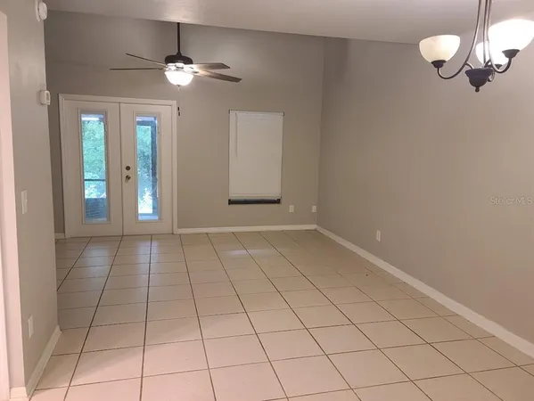 a view of an empty room with window and chandelier fan