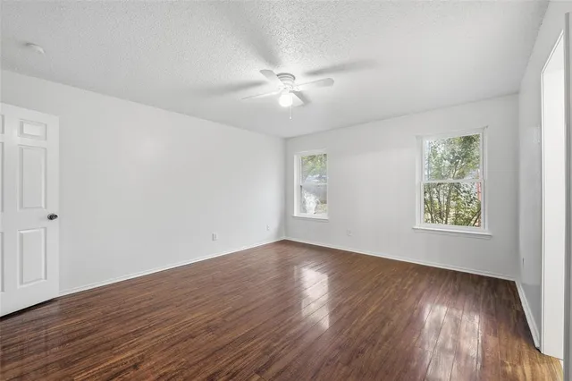 an empty room with wooden floor chandelier fan and windows