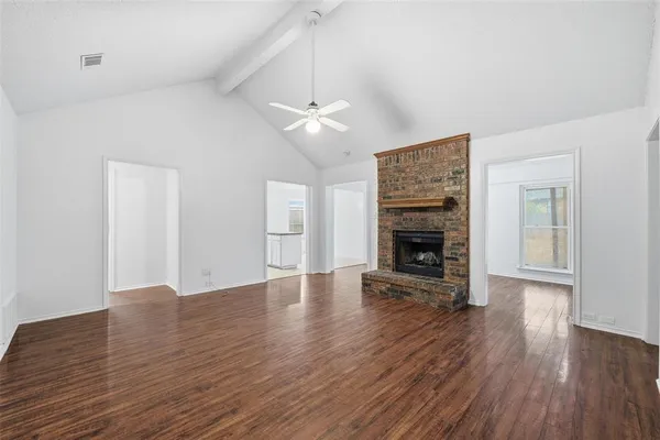 a view of an empty room with wooden floor fireplace and a window