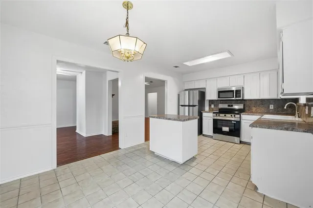 a kitchen with stainless steel appliances granite countertop a refrigerator a stove oven a sink dishwasher and white cabinets with wooden floor