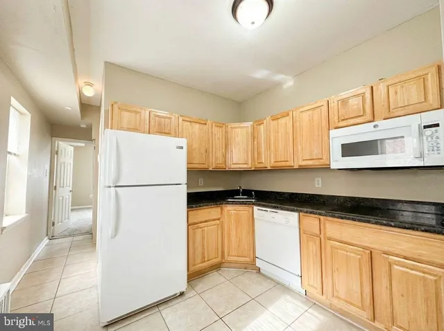 a kitchen with granite countertop a refrigerator a sink and white cabinets