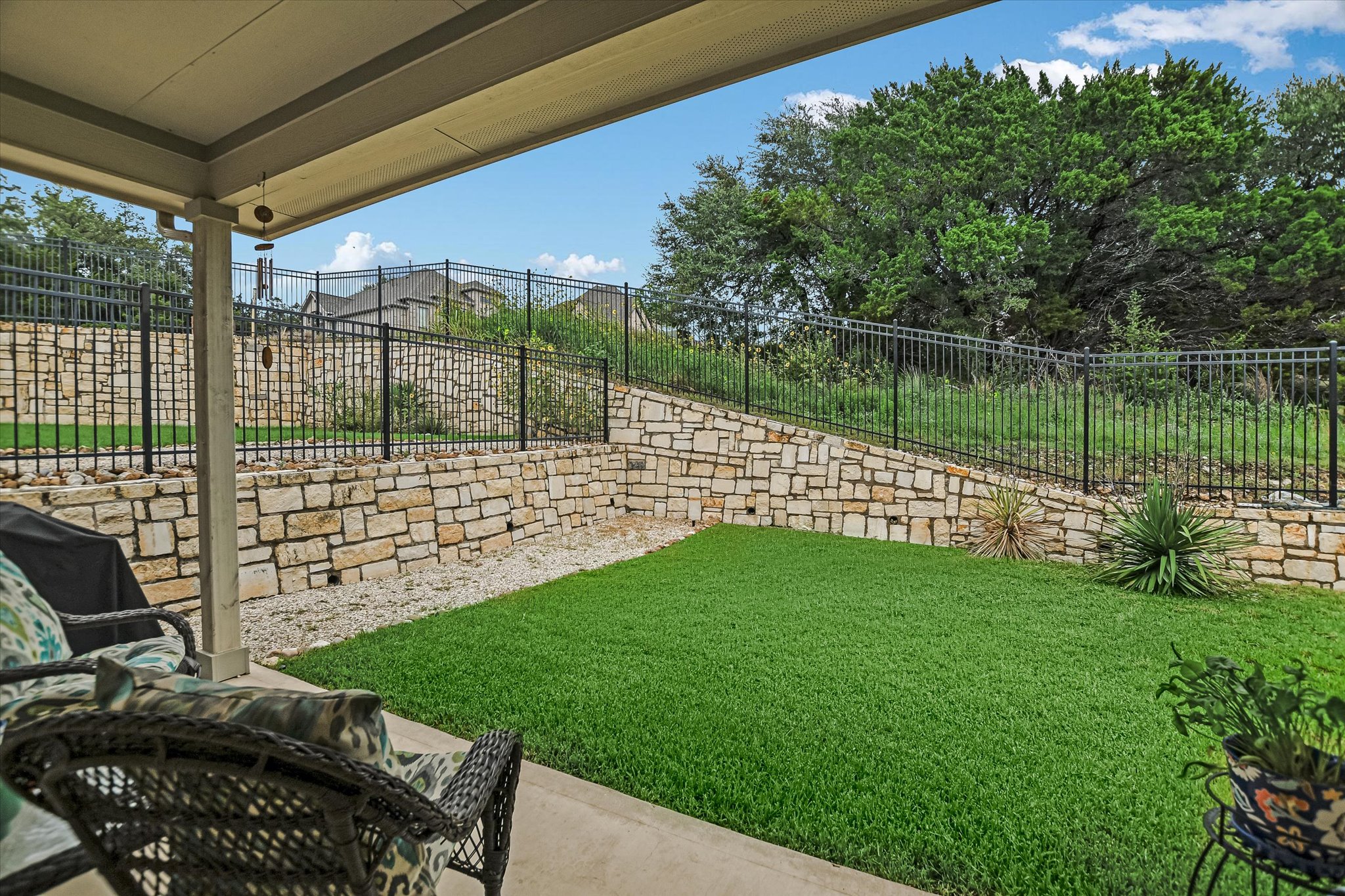 105 Merrick Road Georgetown, TX 78628 - Photo 18 of 23 Relax on the covered patio overlooking a manicured lawn, framed by robust stone retaining walls and secure fencing.