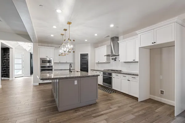 a large kitchen with stainless steel appliances kitchen island granite countertop a large stove a sink dishwasher and a refrigerator with wooden floor