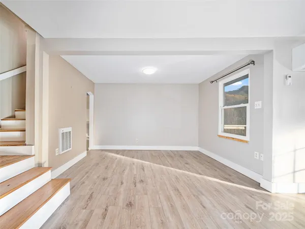 a view of an empty room with wooden floor and a window