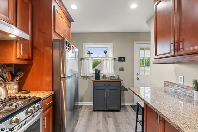 a kitchen with stainless steel appliances granite countertop a refrigerator a sink dishwasher a stove and white countertops with wooden floor