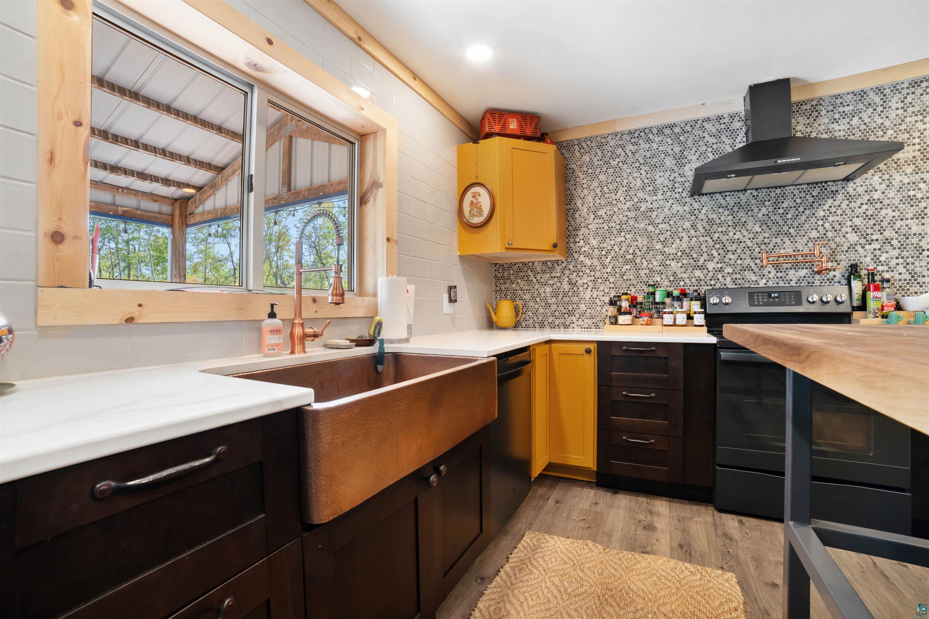 1159 East County Rd B Foxboro, WI 54836 - Photo 11 of 29 Kitchen featuring appliances with stainless steel finishes, light hardwood / wood-style floors, wall chimney exhaust hood, decorative backsplash, and vaulted ceiling with beams