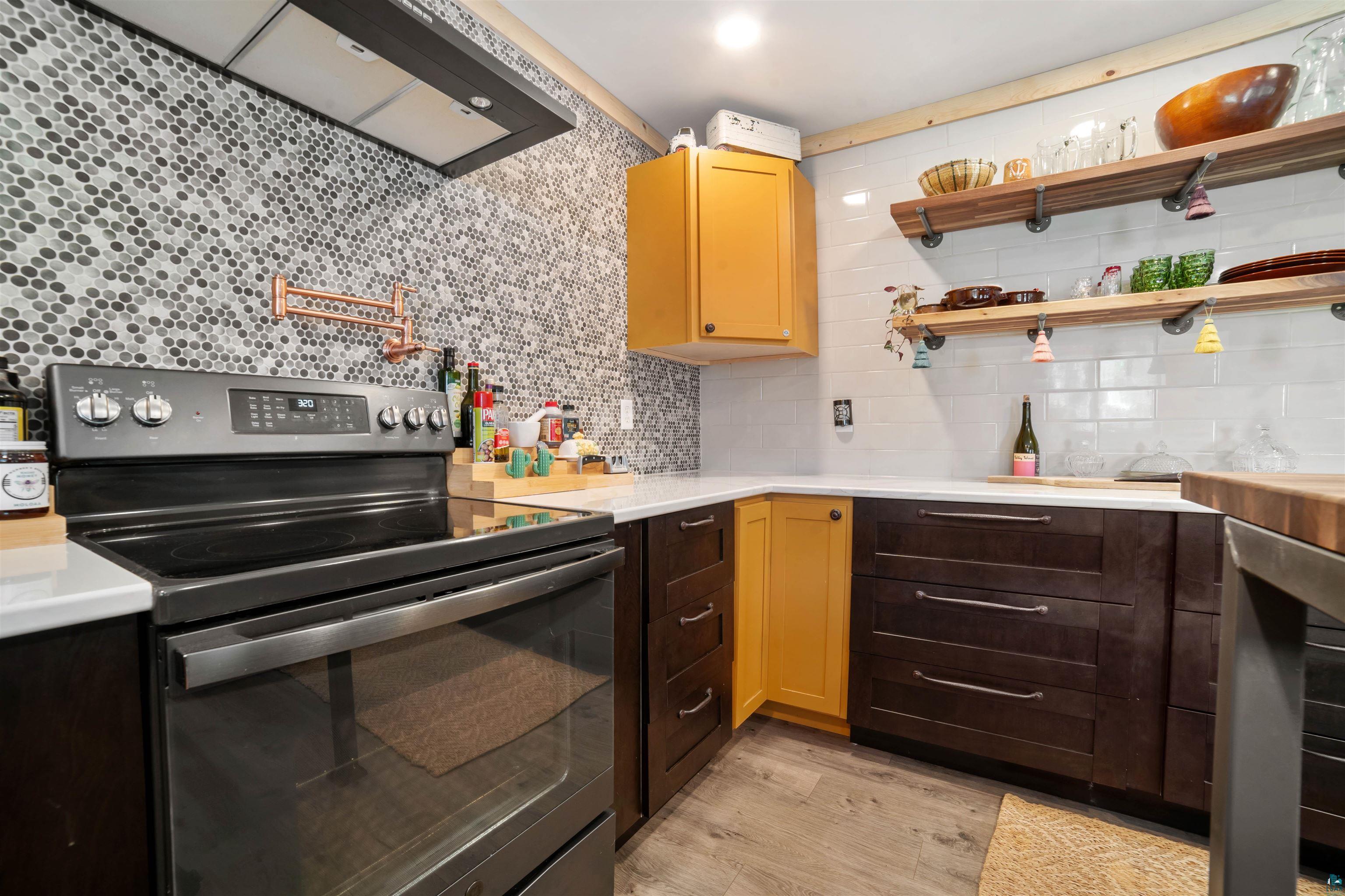 1159 East County Rd B Foxboro, WI 54836 - Photo 12 of 29 Kitchen featuring stainless steel electric range oven, decorative backsplash, wall chimney exhaust hood, and light hardwood / wood-style flooring