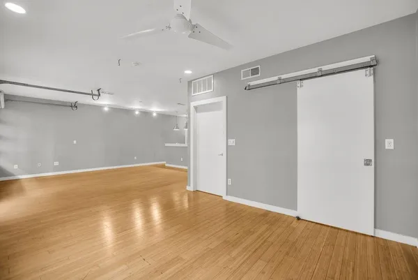 a view of an empty room with wooden floor and a ceiling fan