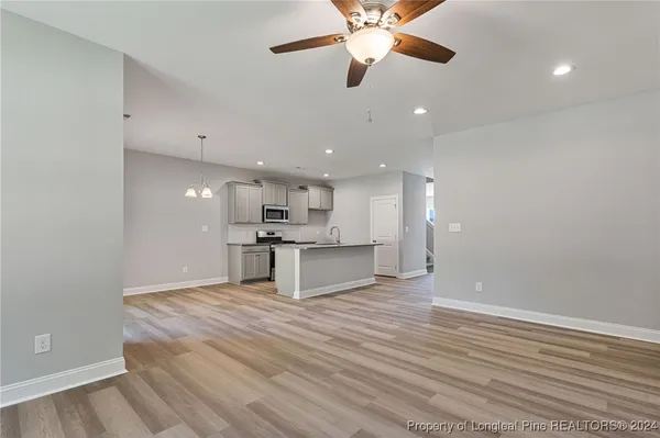 an empty room with wooden floor a ceiling fan and kitchen view