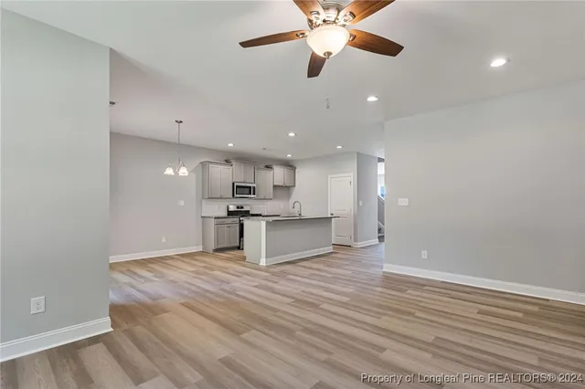 an empty room with wooden floor a ceiling fan and kitchen view