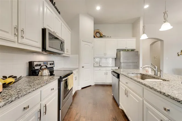 a kitchen with granite countertop a sink stainless steel appliances and white cabinets