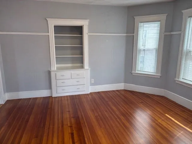 an empty room with wooden floor closet and windows