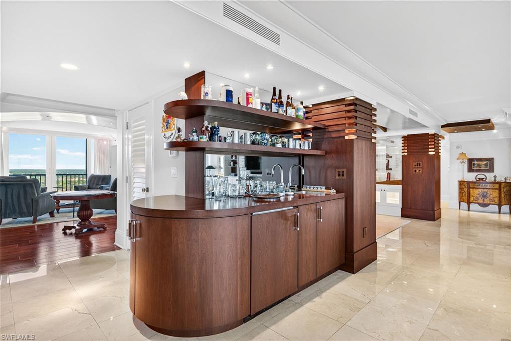 5601 Turtle Bay Drive, Unit 2104 Naples, FL 34108 - Photo 23 of 31 Indoor wet bar featuring open shelves, crown molding, dark countertops, dark brown cabinets, and light marble finish floors