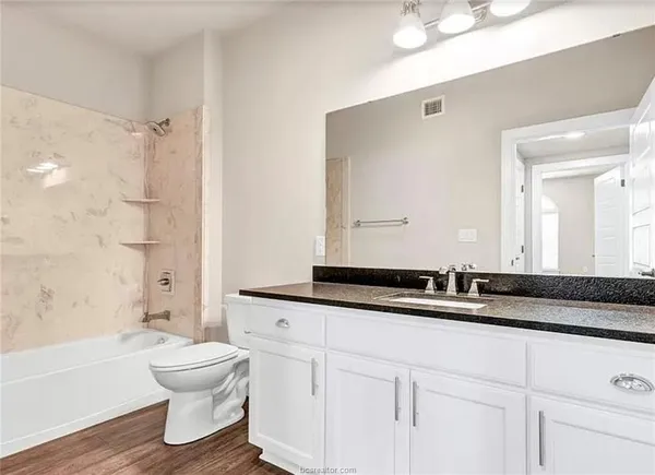 a bathroom with a granite countertop sink a toilet a mirror and bathtub