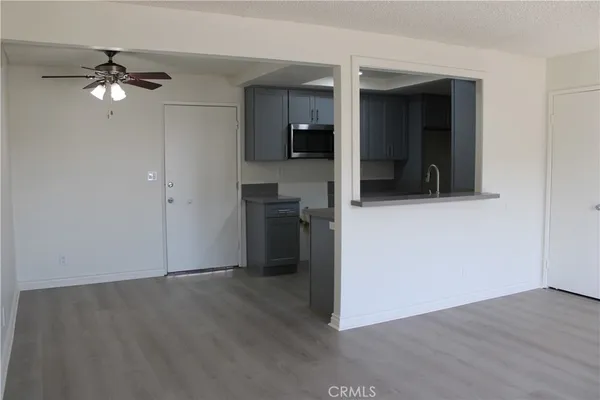 an empty room with wooden floor and way to kitchen
