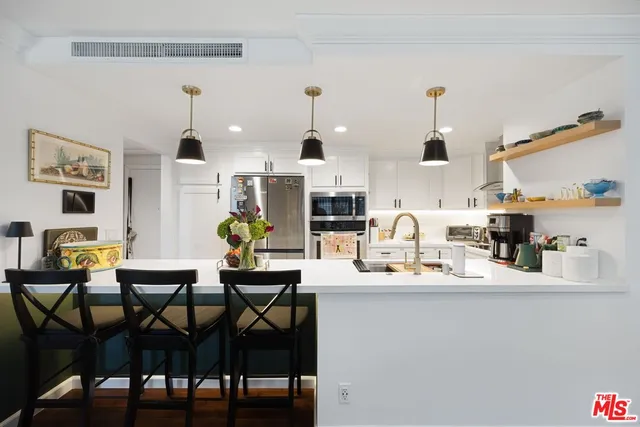 a kitchen with stainless steel appliances kitchen island granite countertop a dining table chairs and a refrigerator