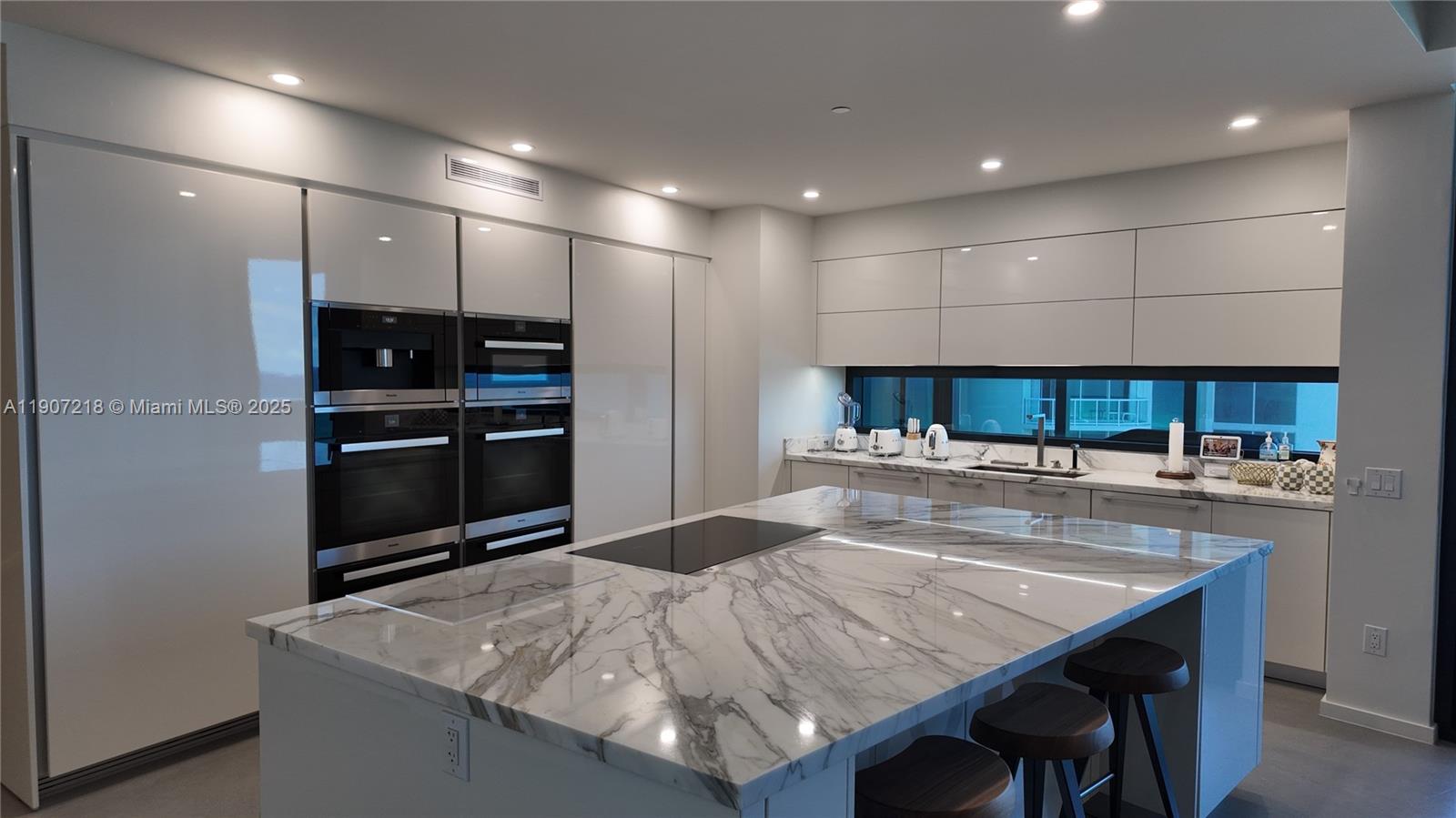 18555 Collins Avenue, Unit 905 Sunny Isles Beach, FL 33160 - Photo 6 of 38 a kitchen with kitchen island a stove and a refrigerator with wooden floor