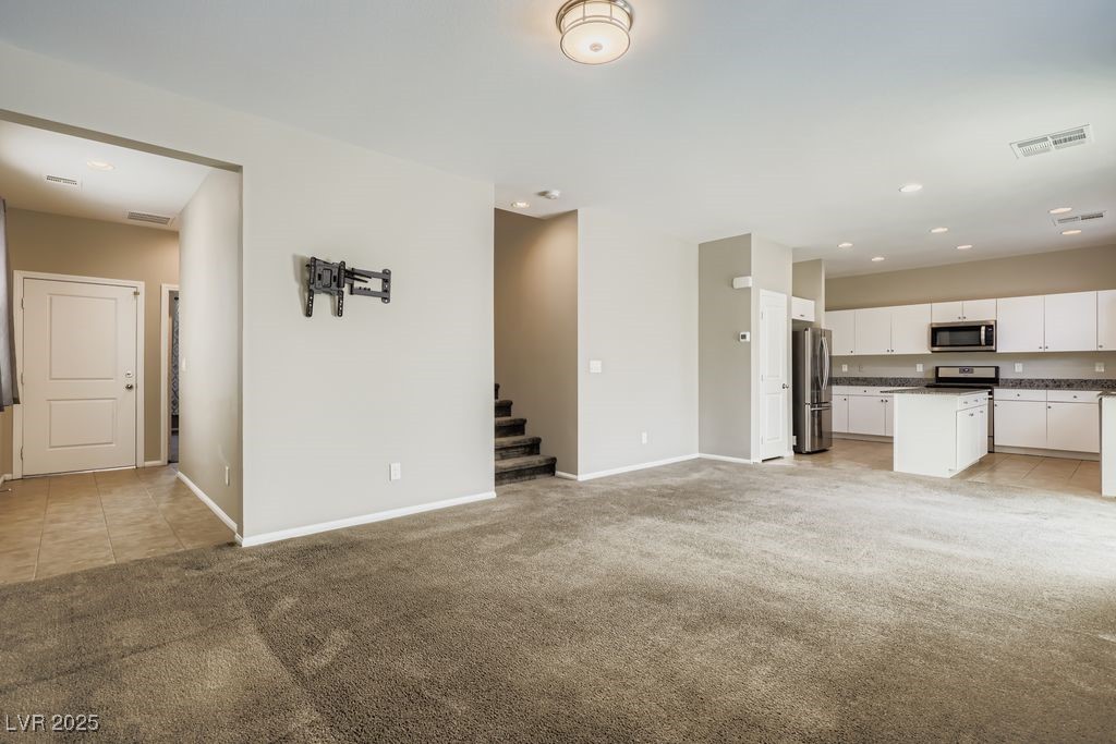 5712 Wishing Coin Court North Las Vegas, NV 89031 - Photo 5 of 24 Unfurnished living room with light colored carpet, recessed lighting, light tile patterned floors, and stairs