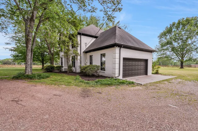 a small white house with a yard and large trees