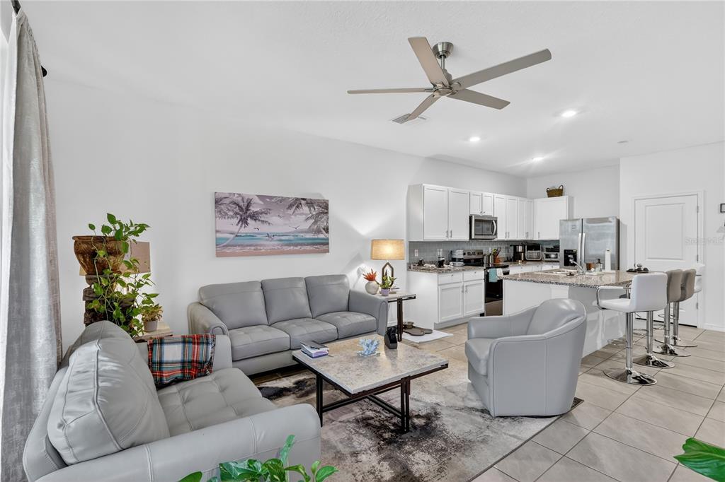 16632 Grotto Steam Place Wimauma, FL 33598 - Photo 6 of 42 a living room with couches a refrigerator and a dining table with wooden floor