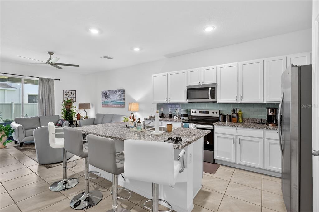 16632 Grotto Steam Place Wimauma, FL 33598 - Photo 9 of 42 a kitchen with stainless steel appliances granite countertop a stove a sink a dining table and chairs