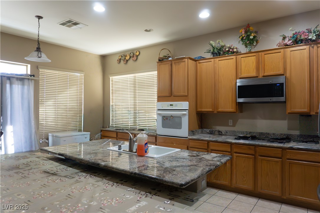6289 Cyclone Avenue Las Vegas, NV 89110 - Photo 11 of 23 Kitchen with dark stone counters, appliances with stainless steel finishes, hanging light fixtures, brown cabinets, and recessed lighting