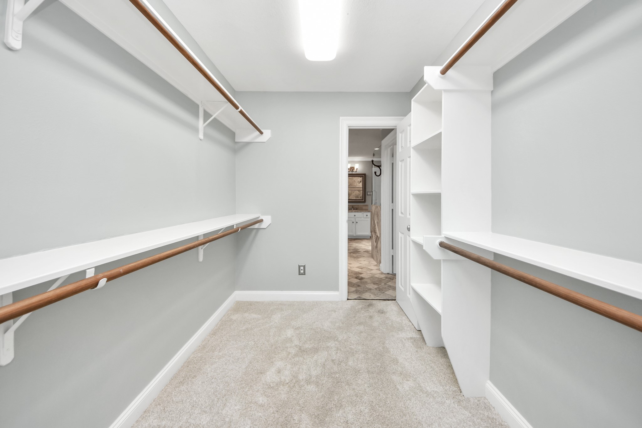 710 Jackson Hill Street Houston, TX 77007 - Photo 25 of 31 Spacious walk-in closet with double hanging rods and open shelving, featuring soft carpet and neutral walls. Brightly lit with an adjoining doorway leading to a tiled area.