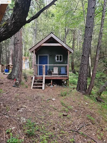 a view of a wooden house with a yard and large trees