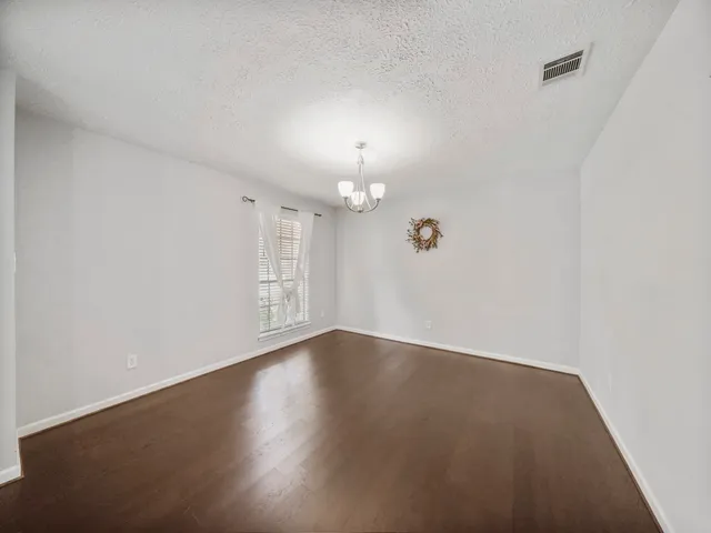 an empty room with wooden floor chandelier fan and windows